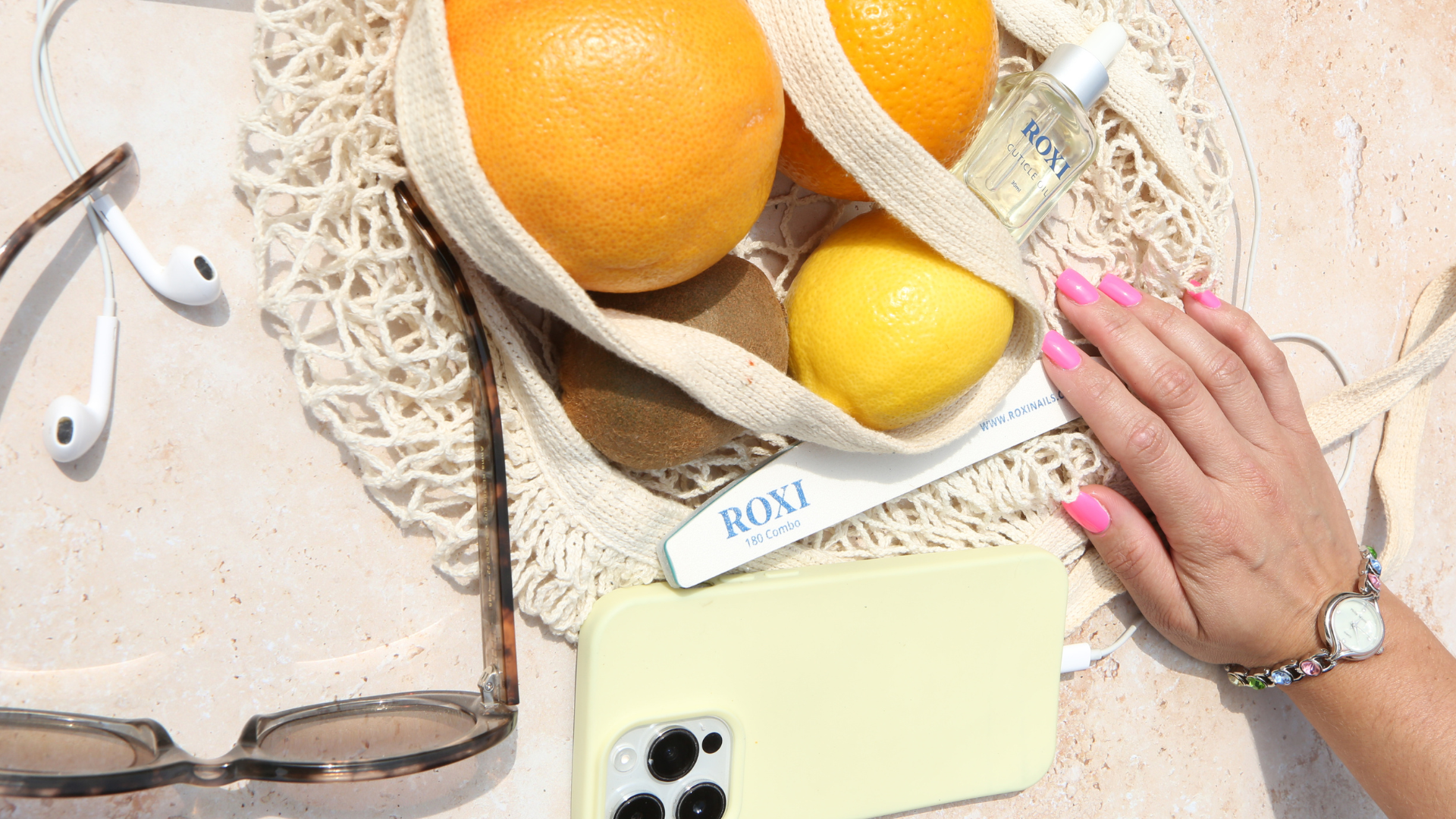 summer styled product shot with a hand with Barbie nail polish on a light stone surface.