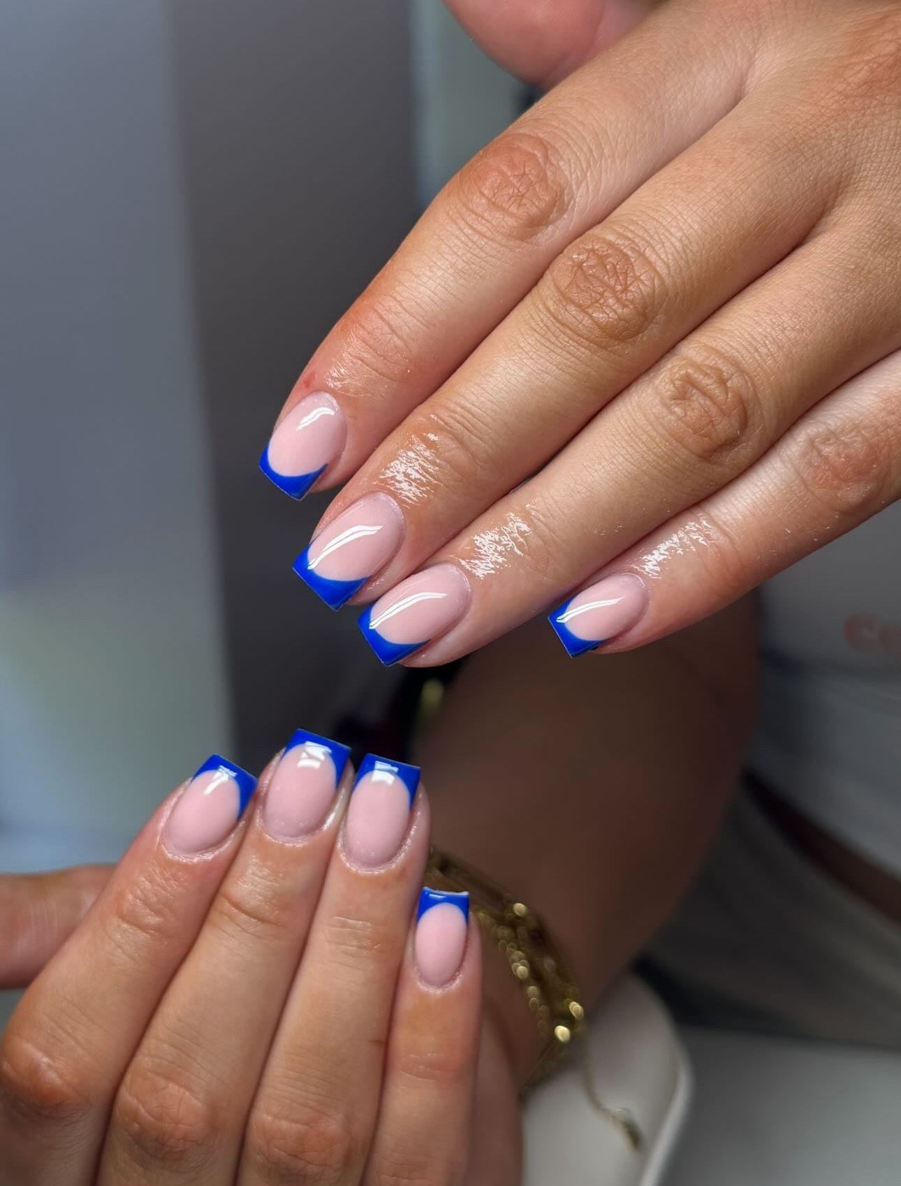 Close-up of manicured fingernails with a pale pink base and bright blue French tips, shown on a person's hands.