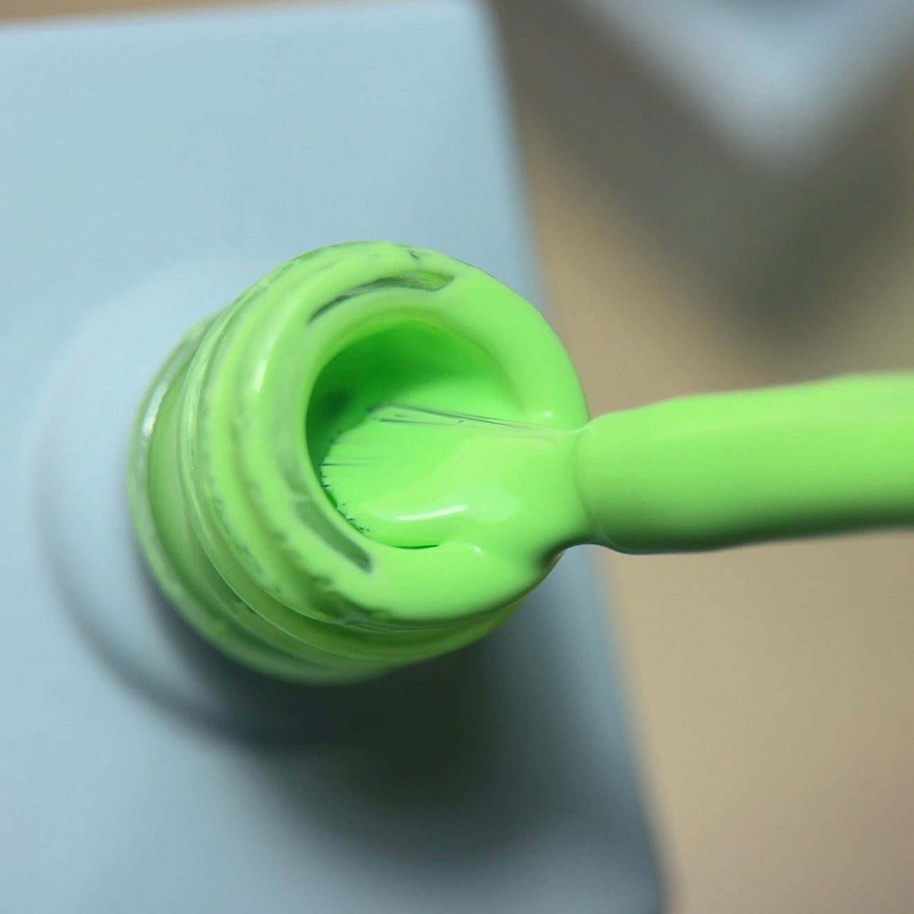 A close-up of a bright neon green nail polish brush resting inside a matching light blue bottle, with the brush handle extending to the right.